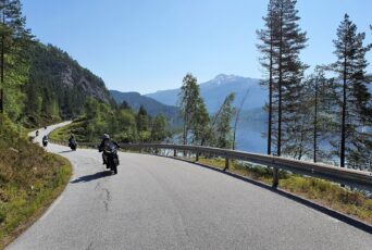 Eine Straße mit Motorradfahrern in Norwegen, die an einem See verläuft